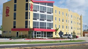 A hotel with a red and yellow facade, multiple windows, and a parking lot with a few cars. - Red Roof Inn & Suites Beaumont (Beaumont)