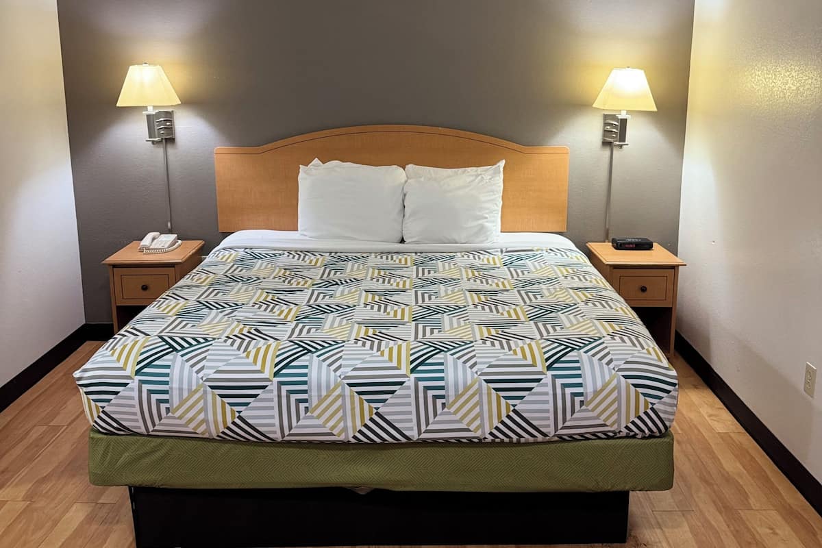 A hotel room with a large bed, two bedside tables, two lamps, and a ceiling-mounted smoke detector.