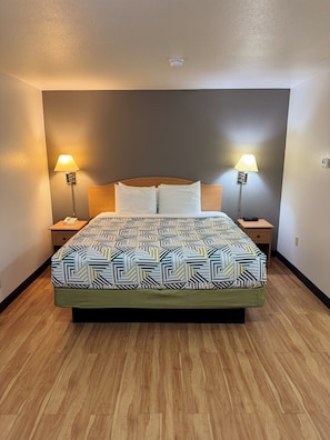 A neatly arranged hotel room with a large bed, two bedside lamps, a telephone, and a wall-mounted light fixture. - Blue Bonnet Suites Extended Stay Lubbock, Texas (Lubbock)