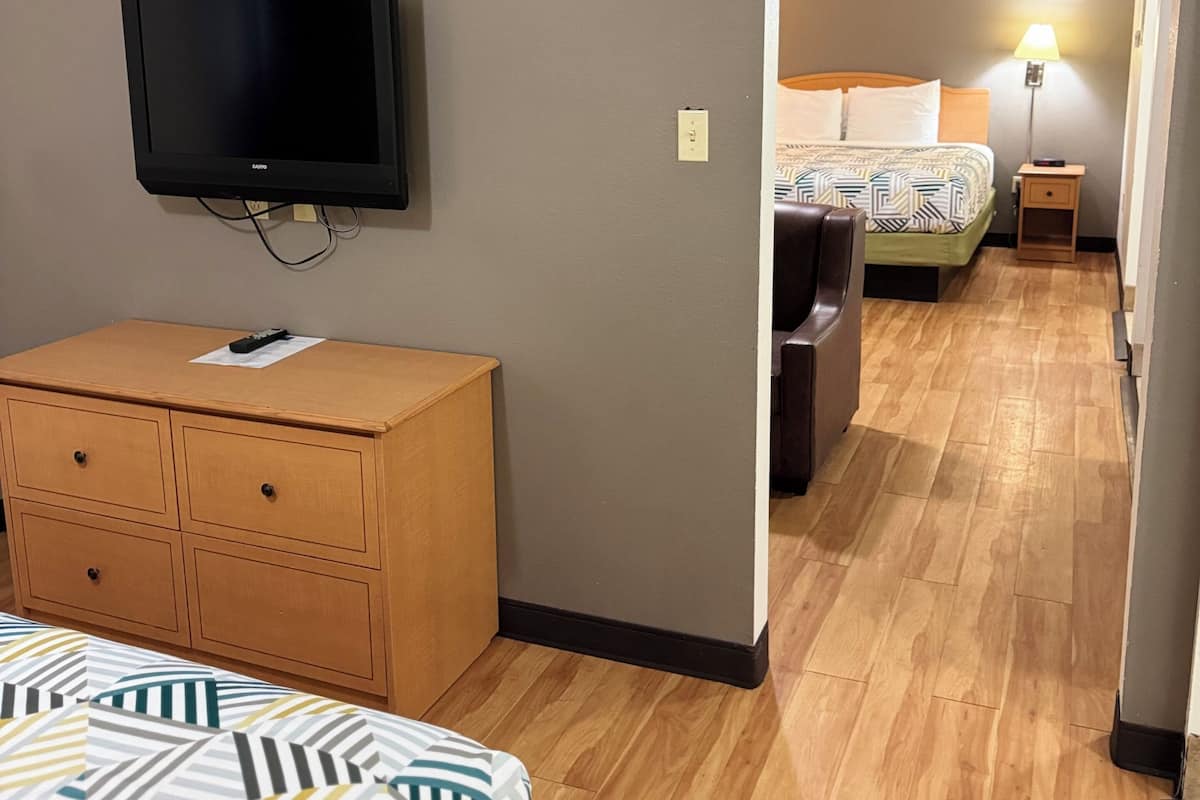 A hotel room with a bed, a wooden dresser, a television mounted on the wall, and a nightstand with a lamp.
