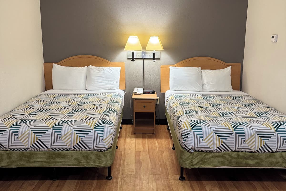 A twin room with two beds, each with patterned bedding, a nightstand, and two wall-mounted lamps.