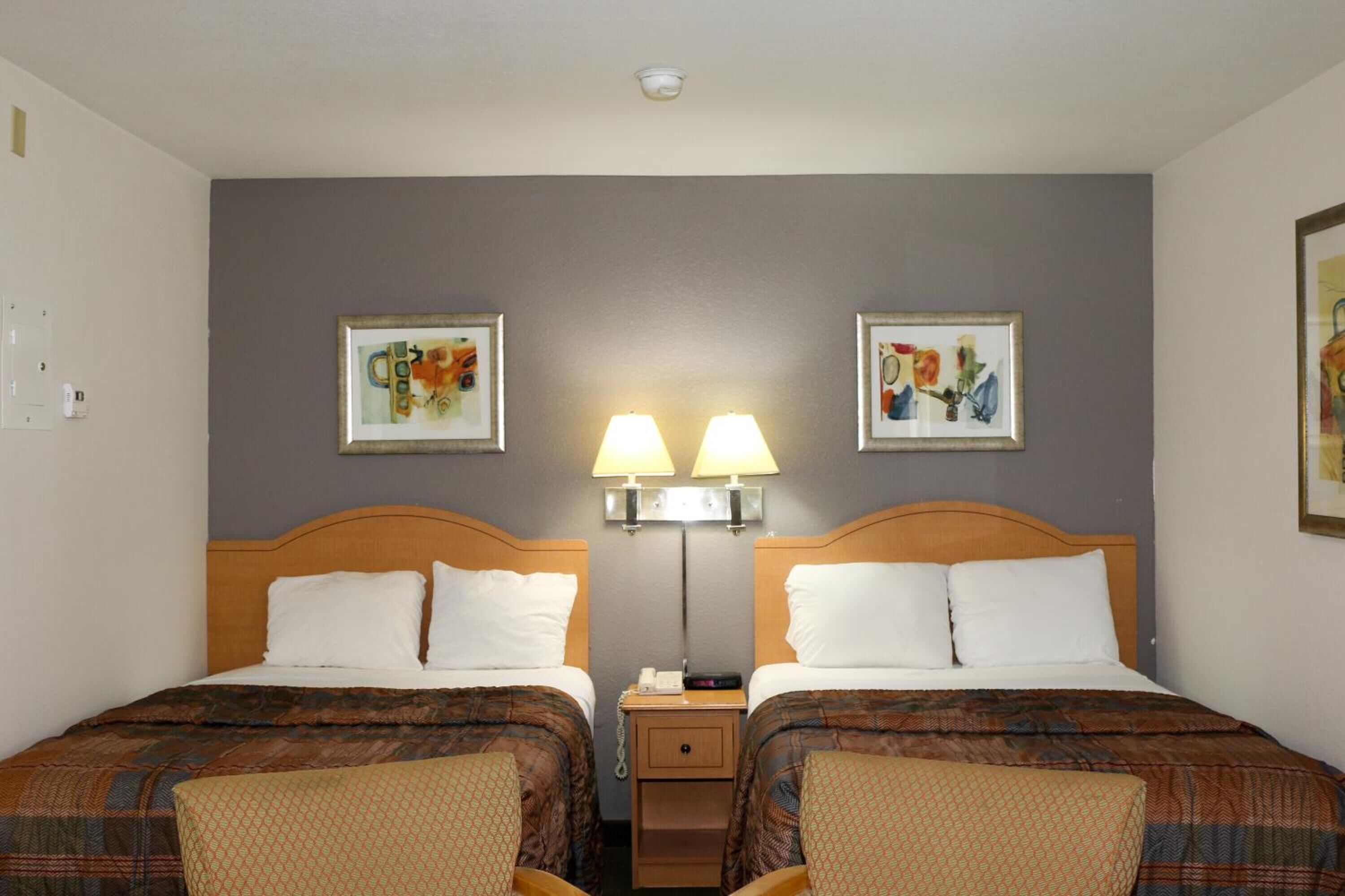 A hotel room with two beds, a nightstand with lamps, and two framed artworks on the wall.