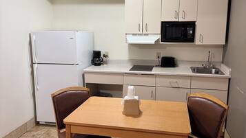 A compact kitchen with a refrigerator, microwave, and sink. There is a wooden table with two chairs and a small white object on it.