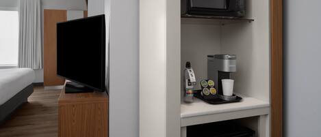 A hotel room with a flat-screen TV, a coffee machine, and a microwave on a white countertop.