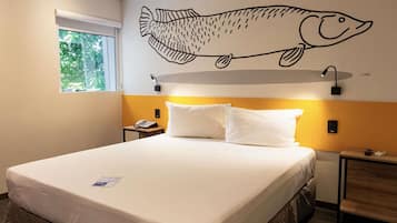 Quarto de hotel com uma cama, um mural de peixe na parede, luminárias de cabeceira e uma janela com vista para vegetação.