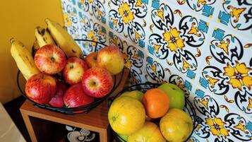 Un frutero con manzanas y plátanos sobre una mesa frente a una pared estampada.