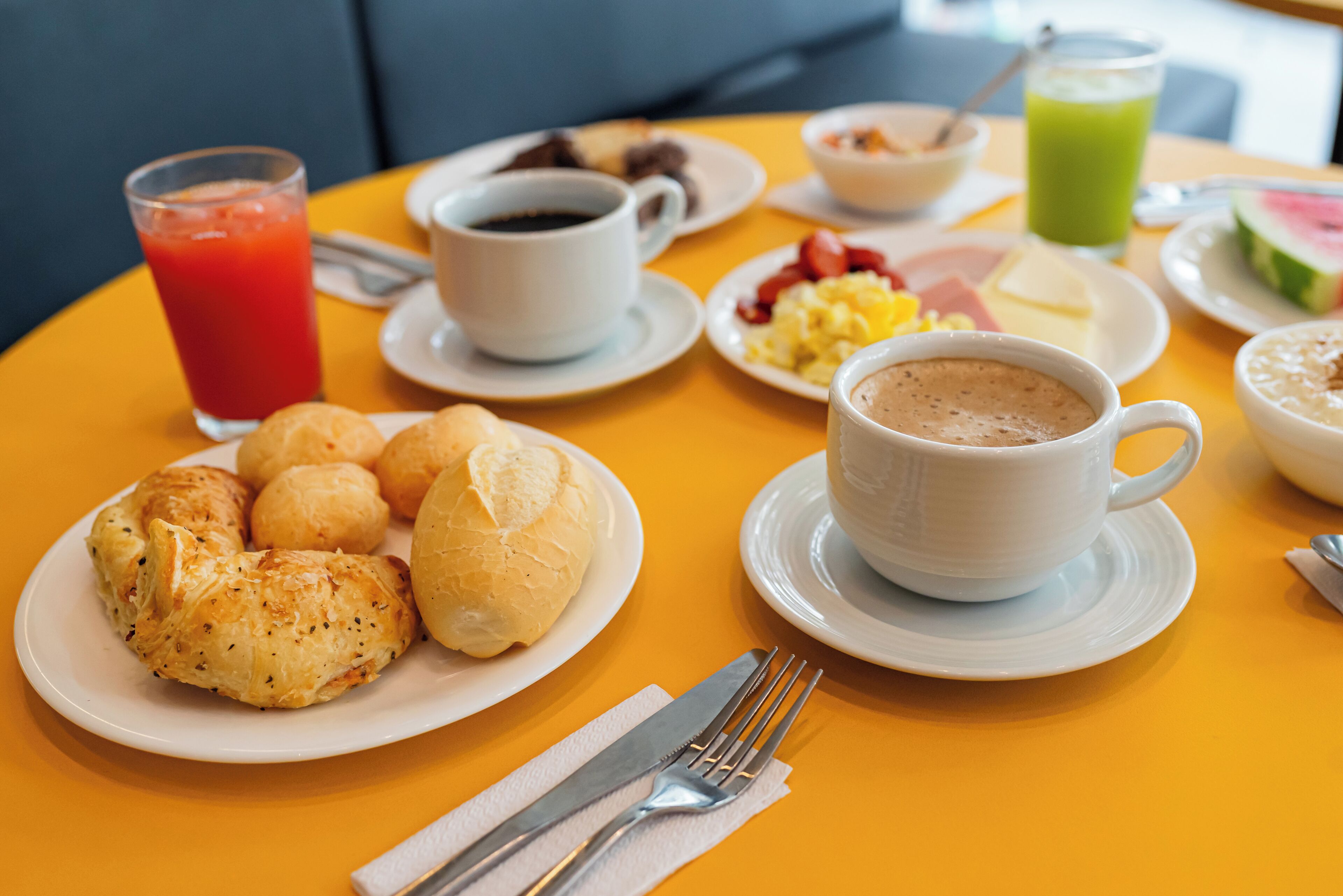 A breakfast table with croissants, a cup of coffee, a glass of juice, and various other breakfast items.