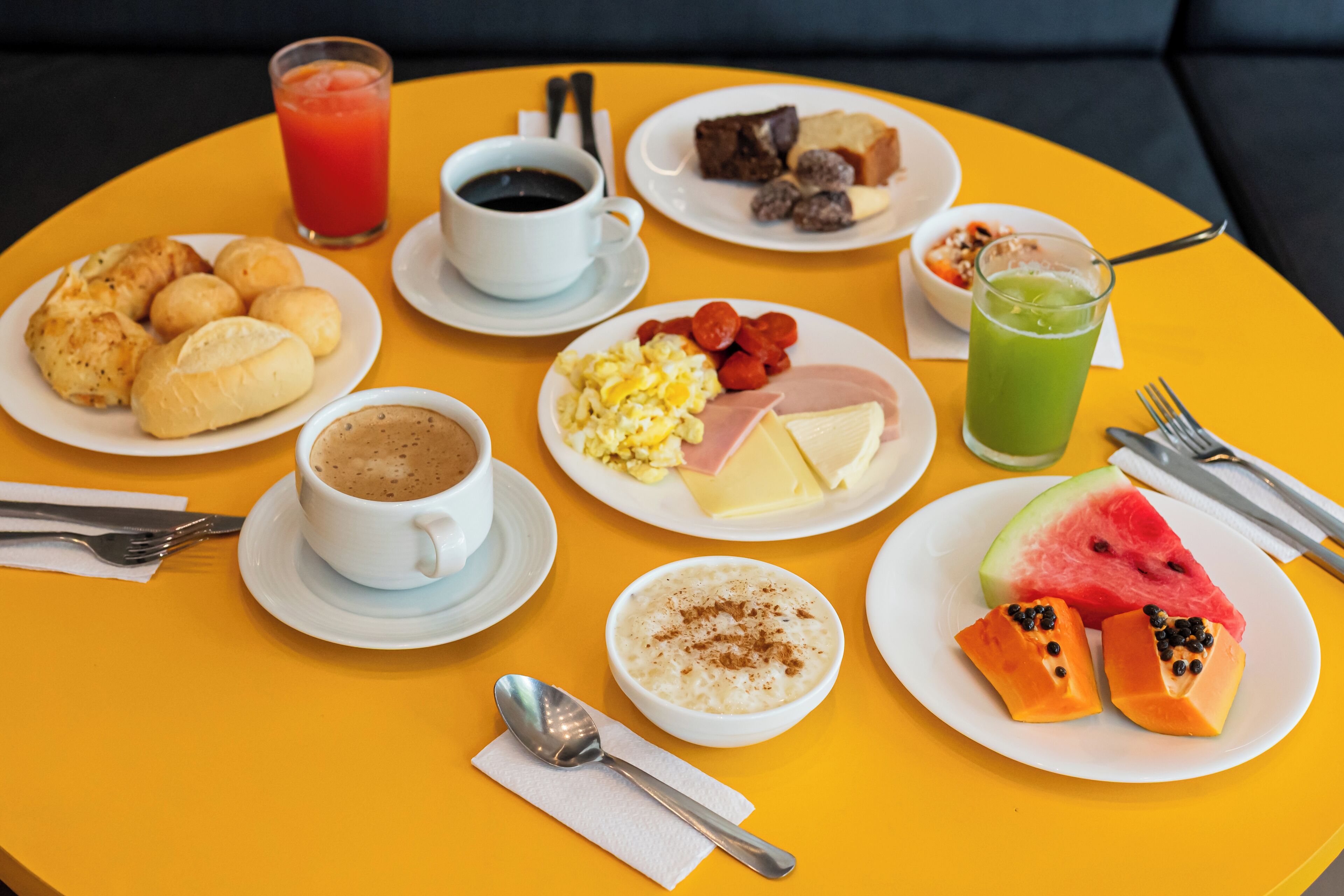 A yellow table with breakfast items including croissants, eggs, ham, and watermelon.