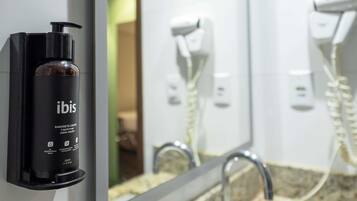 A bathroom with a black bottle of Ibis liquid soap, a mirror, a sink, and a hairdryer.