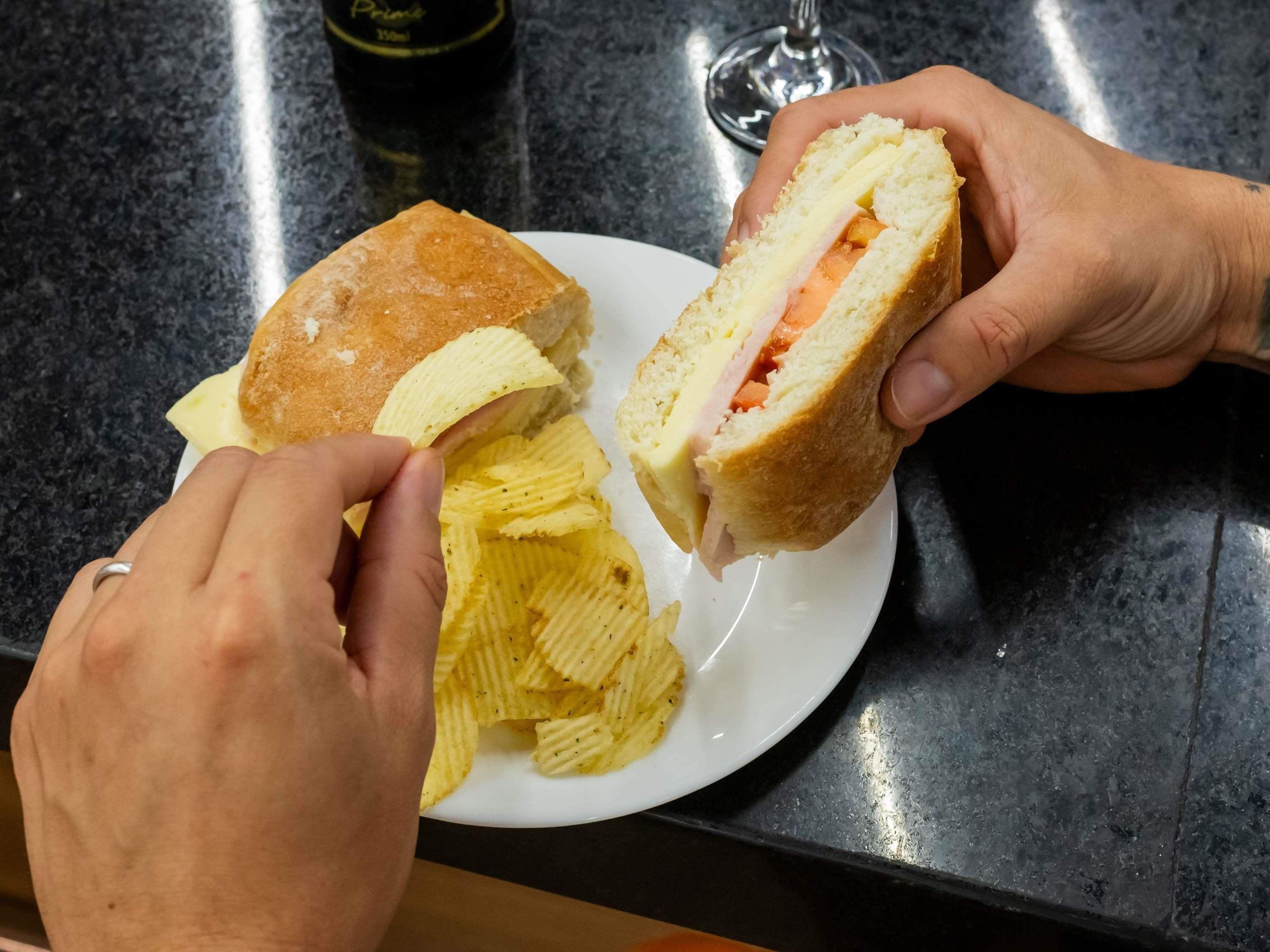 A sandwich cut in half with visible fillings, a plate of chips, and a glass of beverage on a countertop.