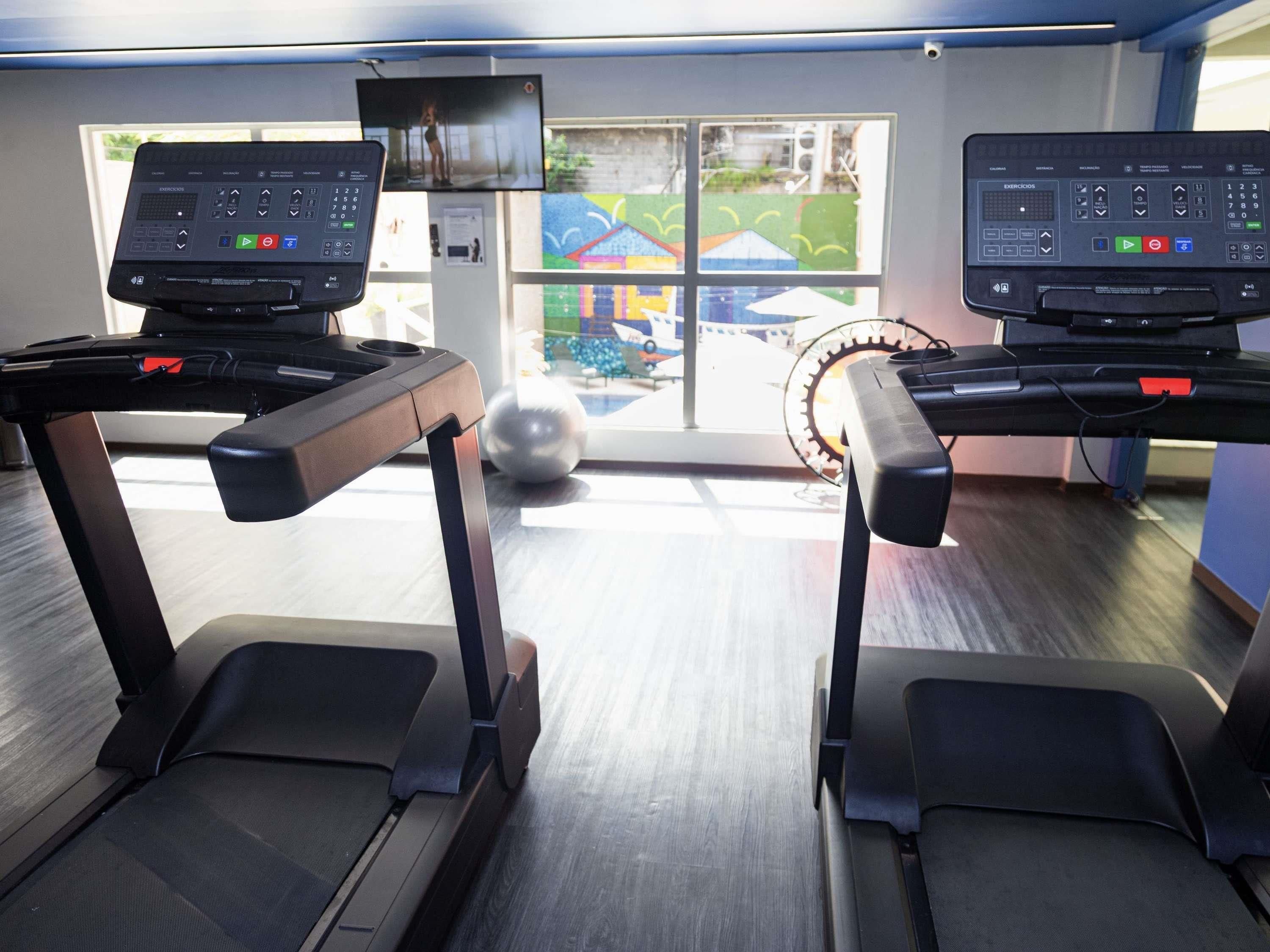 Two treadmills with digital displays, a large window with a view of a playground, and a stationary bike.