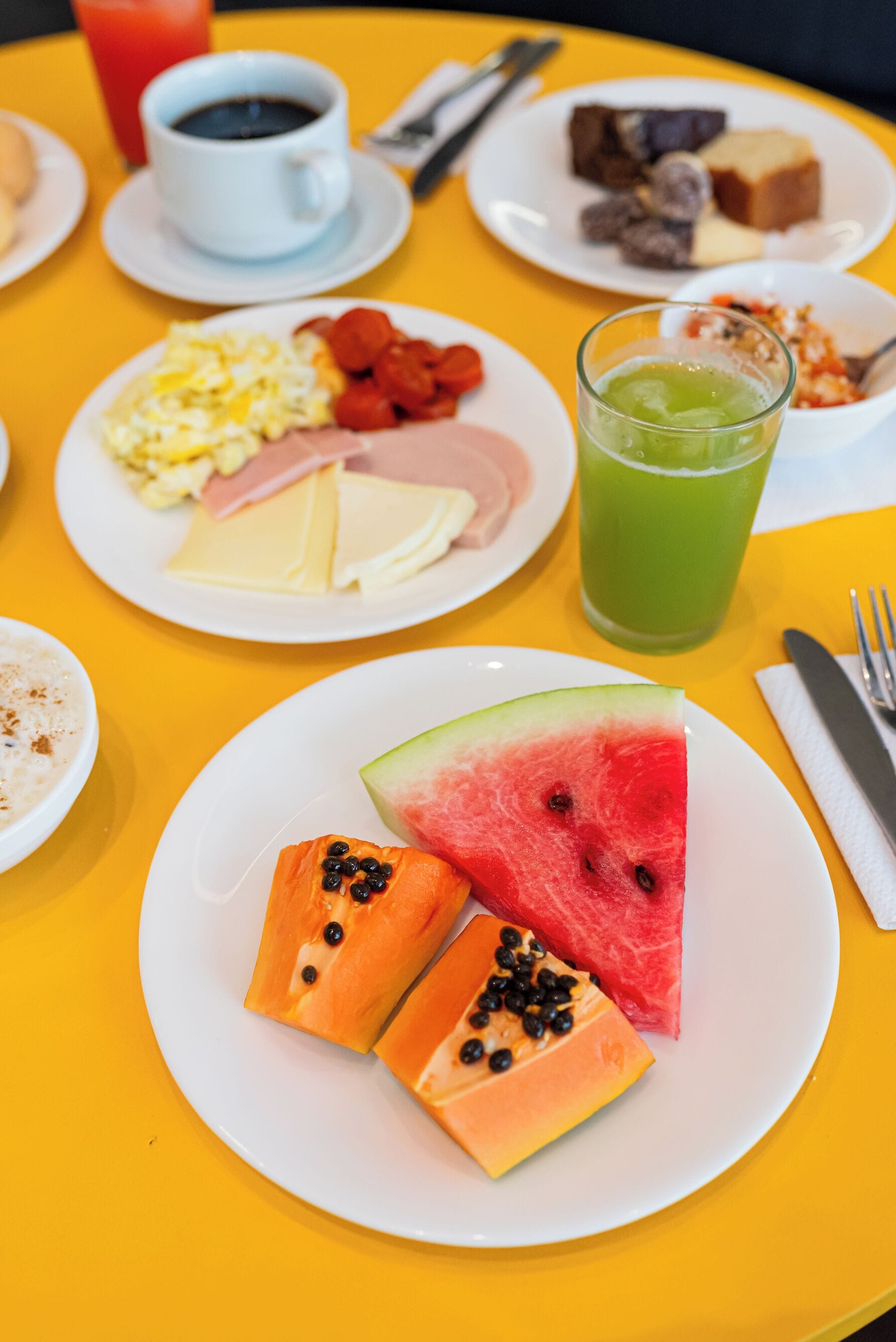 Una mesa con diferentes opciones de desayuno, como huevos, jamón, queso y fruta.