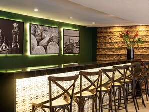 A bar area with a green wall, framed pictures, and a stone wall backdrop. - ibis Styles Belém Nazaré (Belém)
