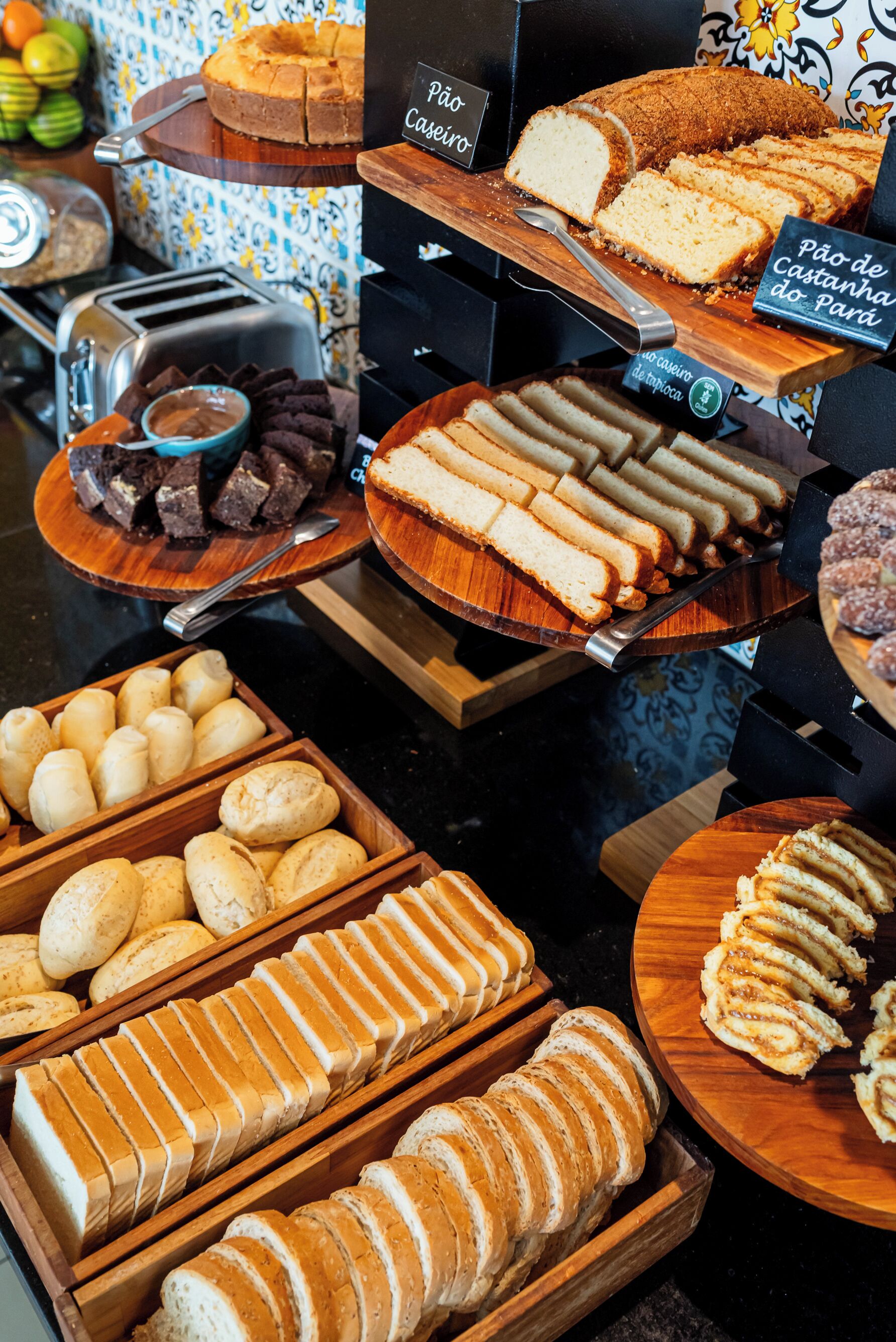 A variety of baked goods displayed on wooden boards and trays, including bread, cakes, and pastries.