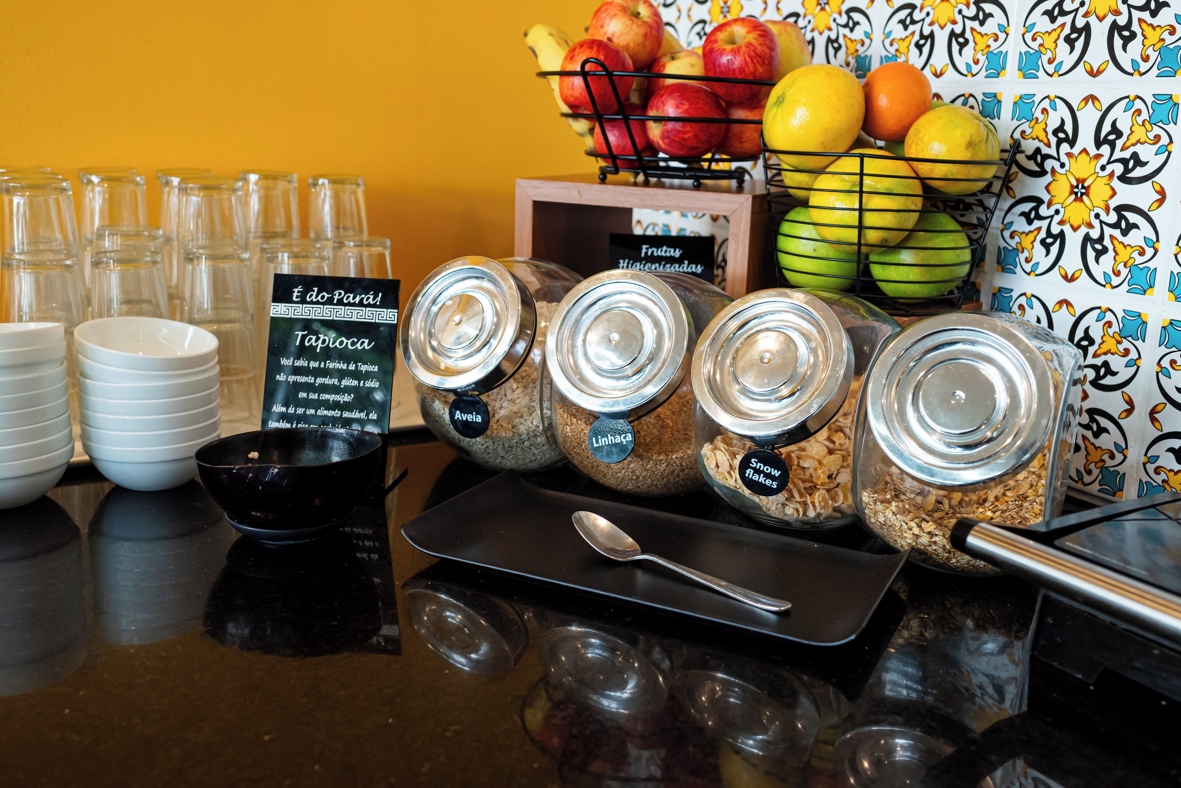 Un buffet de petit-déjeuner avec des récipients à aliments étiquetés, un saladier de fruits et des bols empilés.