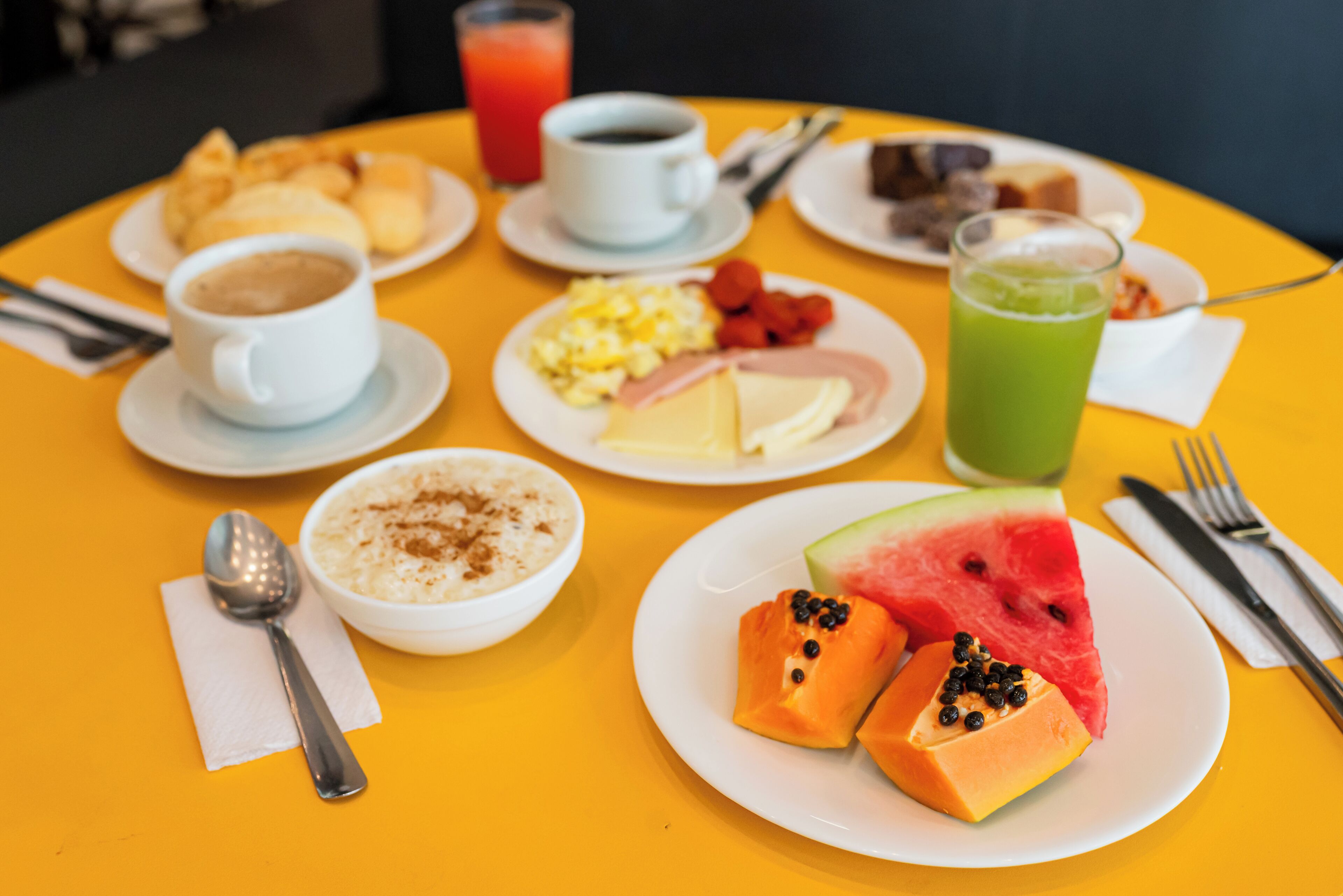 Una mesa de desayuno con diversos platos, incluyendo huevos, tostadas, fruta y bebidas.