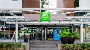Een hotelentree met een glazen gevel, een bord met 'ibis Styles Hotels' en een muurschildering van een blauwe papegaai.
