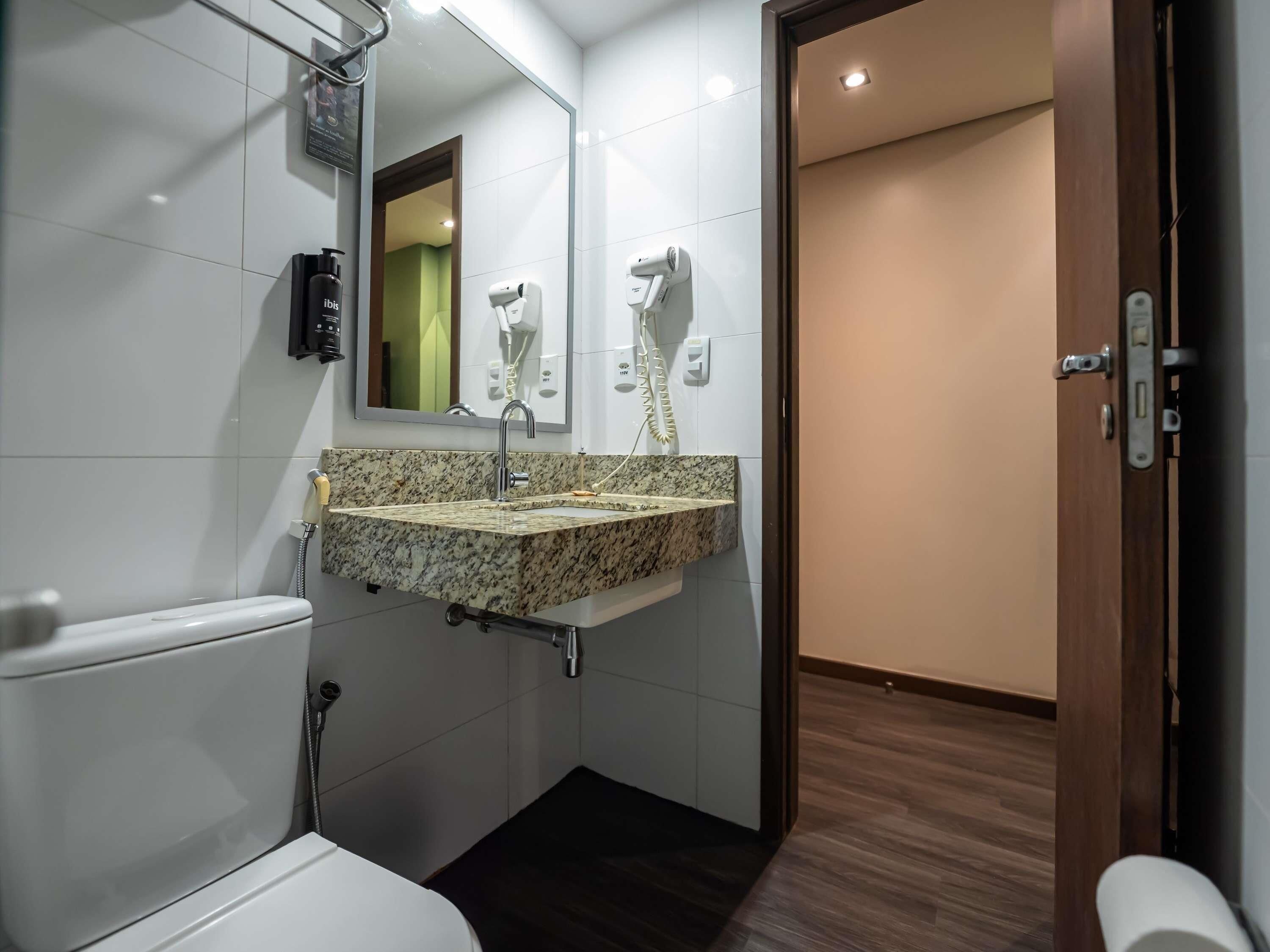 A bathroom with a marble sink, a handheld showerhead, a hairdryer, and a toilet.