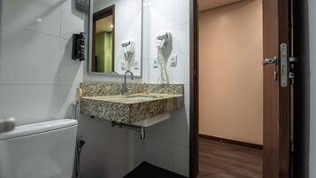 A bathroom with a marble sink, a handheld showerhead, a hairdryer, and a toilet.
