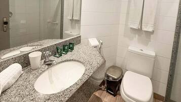 Un baño moderno con lavamanos de granito, inodoro, ducha y un espejo grande.