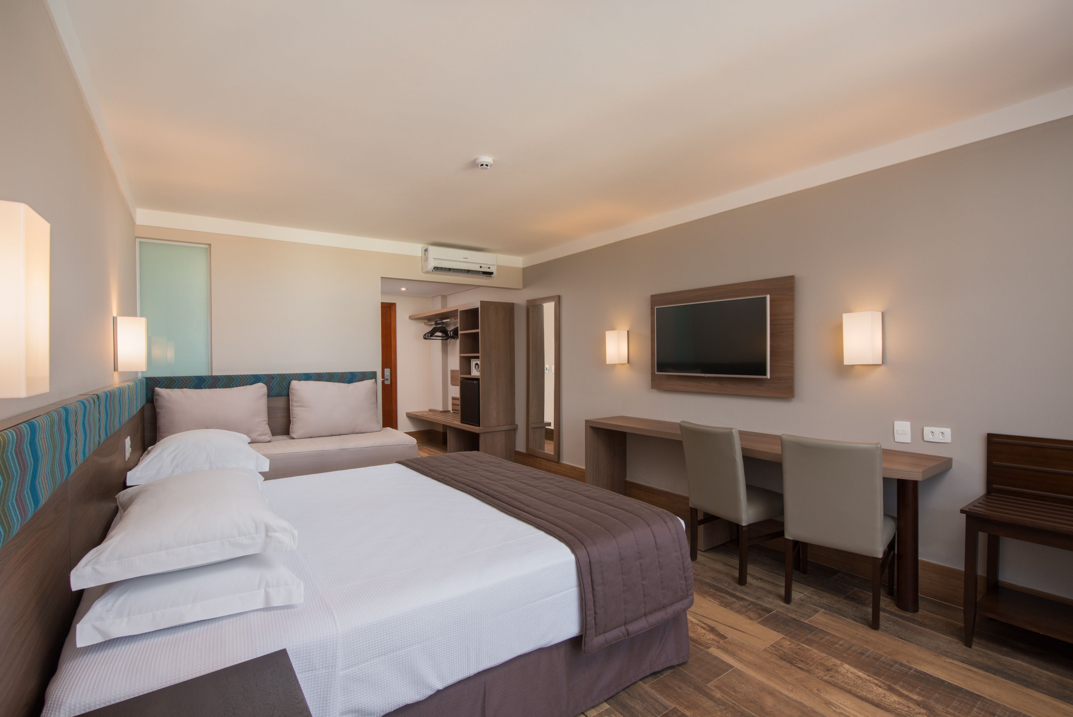 A hotel room with two beds, a desk, a chair, a TV, and a wardrobe.