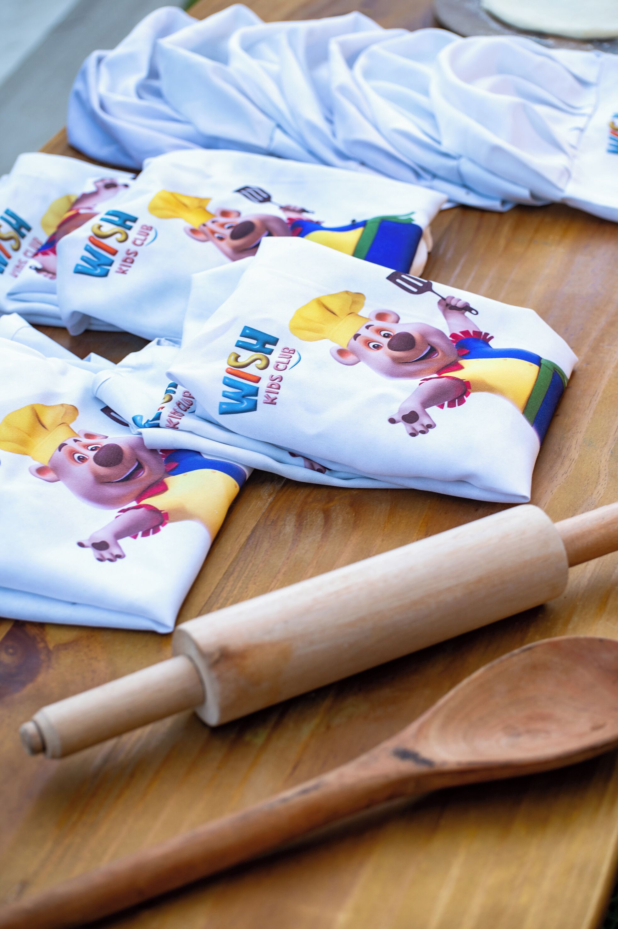 Superficie de madera con rollos de tela blanca que muestran un personaje de dibujos animados y el texto 'WISH KIDS CLUB'.