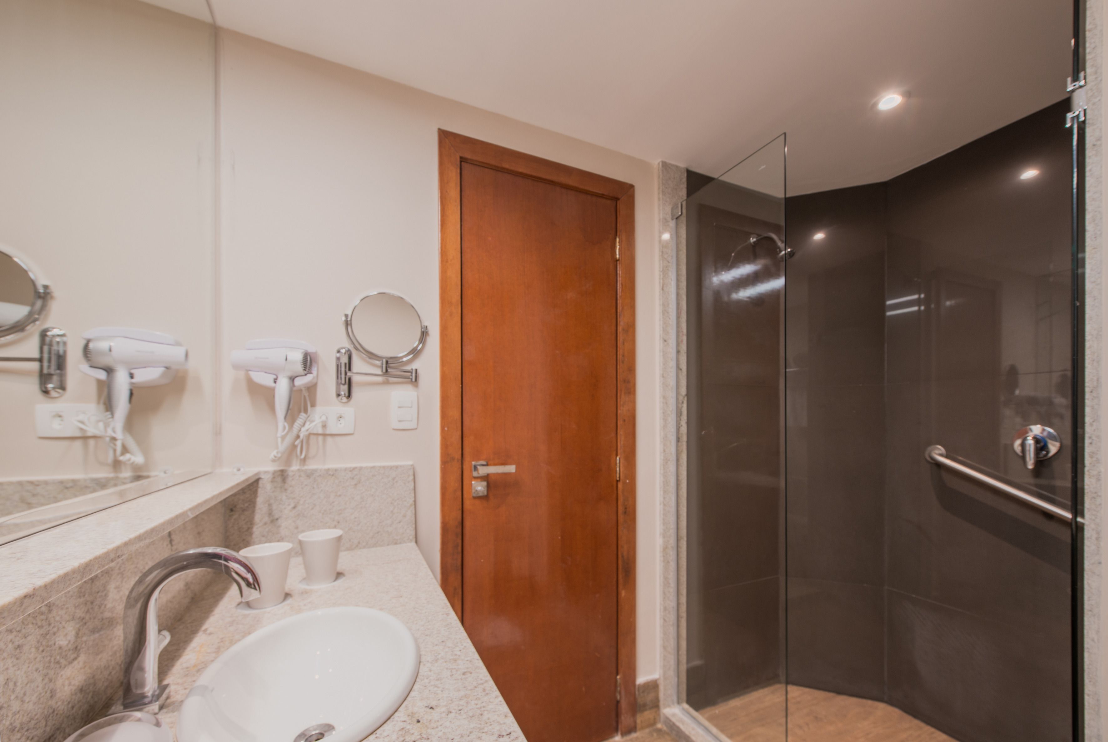 A bathroom with a sink, mirrors, hair dryers, and a glass shower enclosure.