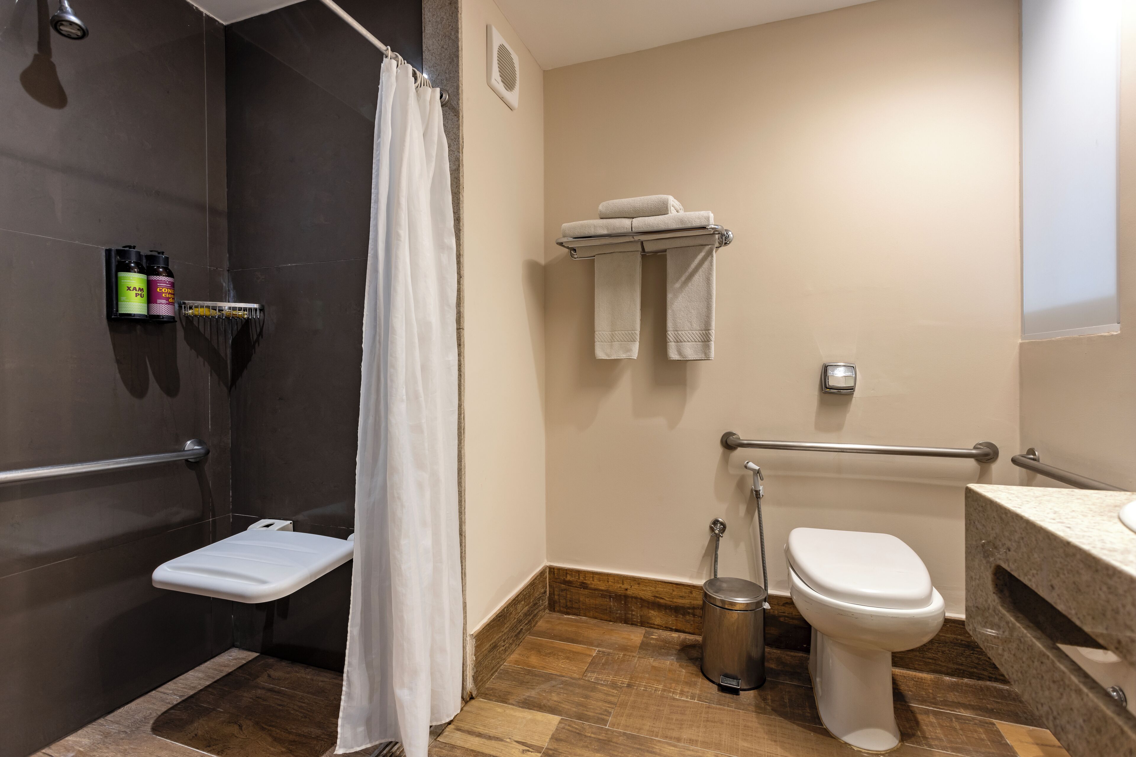 Une salle de bain avec une douche, des toilettes et un lavabo. On y trouve deux serviettes sur un porte-serviettes, un rideau de douche et une étagère avec des articles de toilette.