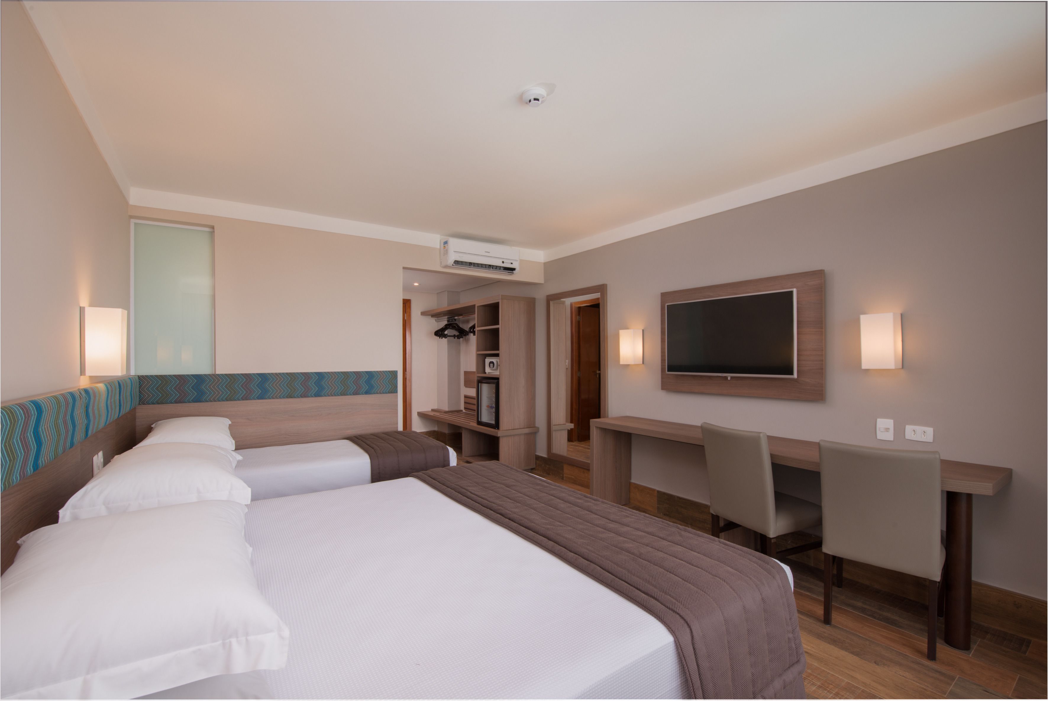 A hotel room with two beds, a desk, a TV, and a wardrobe.