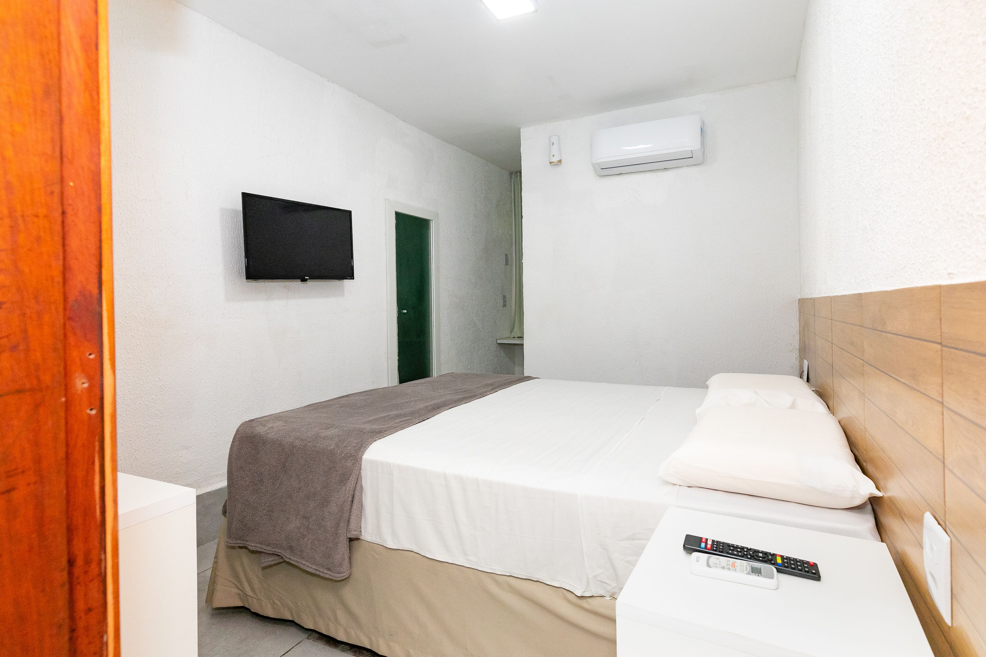 Una habitación de hotel con una cama, un televisor montado en la pared y un equipo de aire acondicionado.