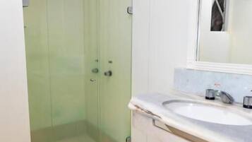 Un baño con cabina de ducha de vidrio, un lavabo blanco y un espejo encima, además de un inodoro.