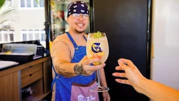 A person in a blue apron holding a drink with a logo, standing in a room with a counter and a door.
