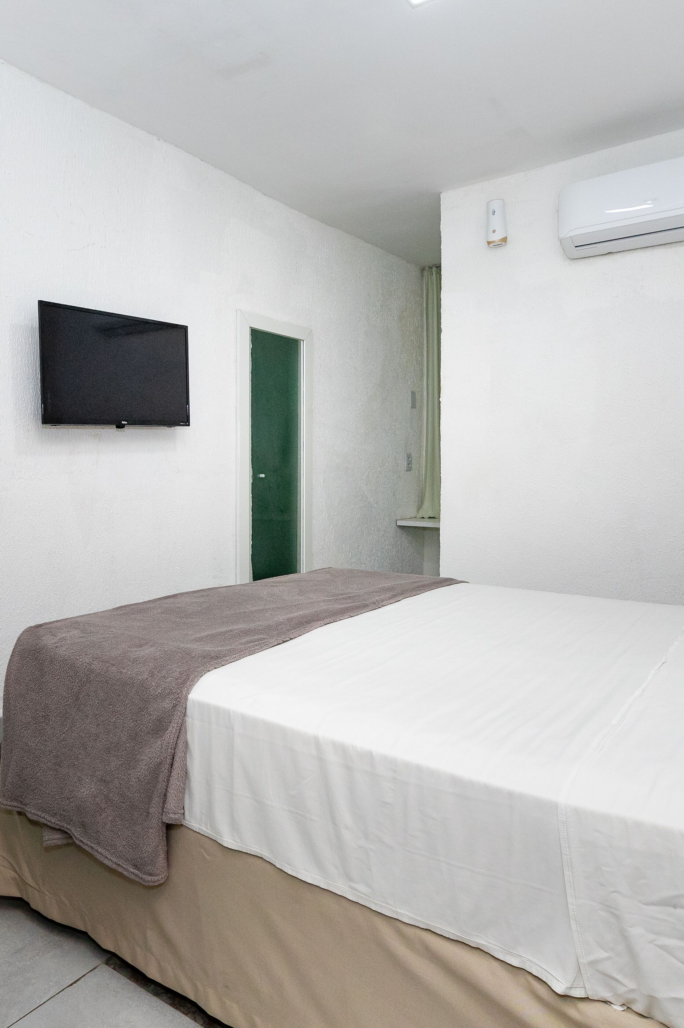 Ein Hotelzimmer mit einem Bett, einem an der Wand montierten Fernseher, einer Klimaanlage und einer grünen Tür.