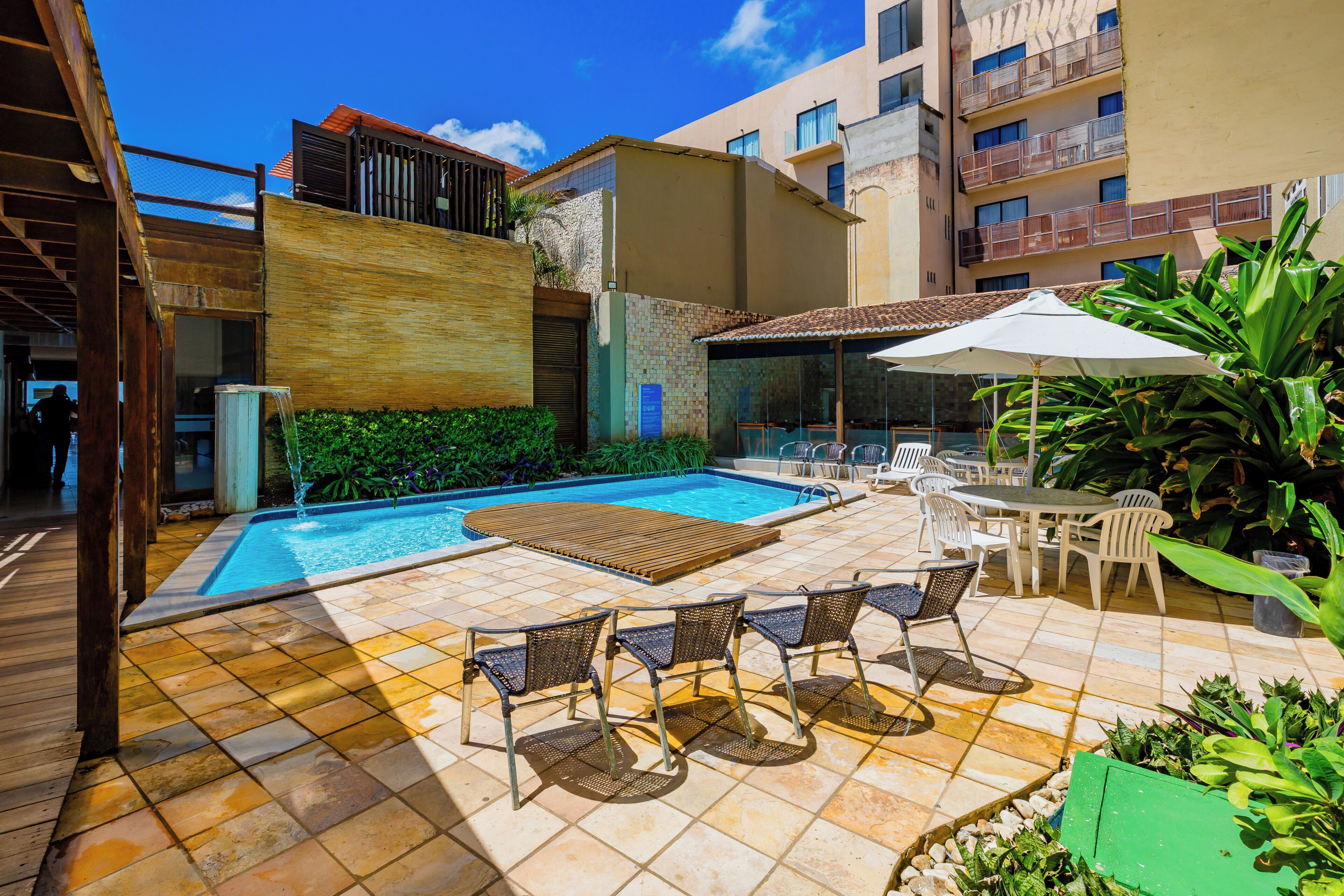 A swimming pool with lounge chairs and a table, surrounded by greenery and a tiled patio.