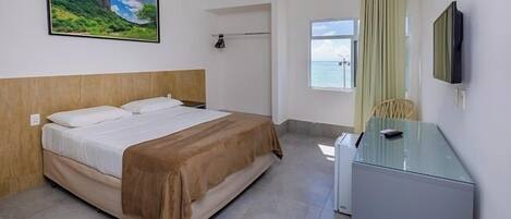 A hotel room with a bed, a desk, a TV, a window with a view, and a painting on the wall.