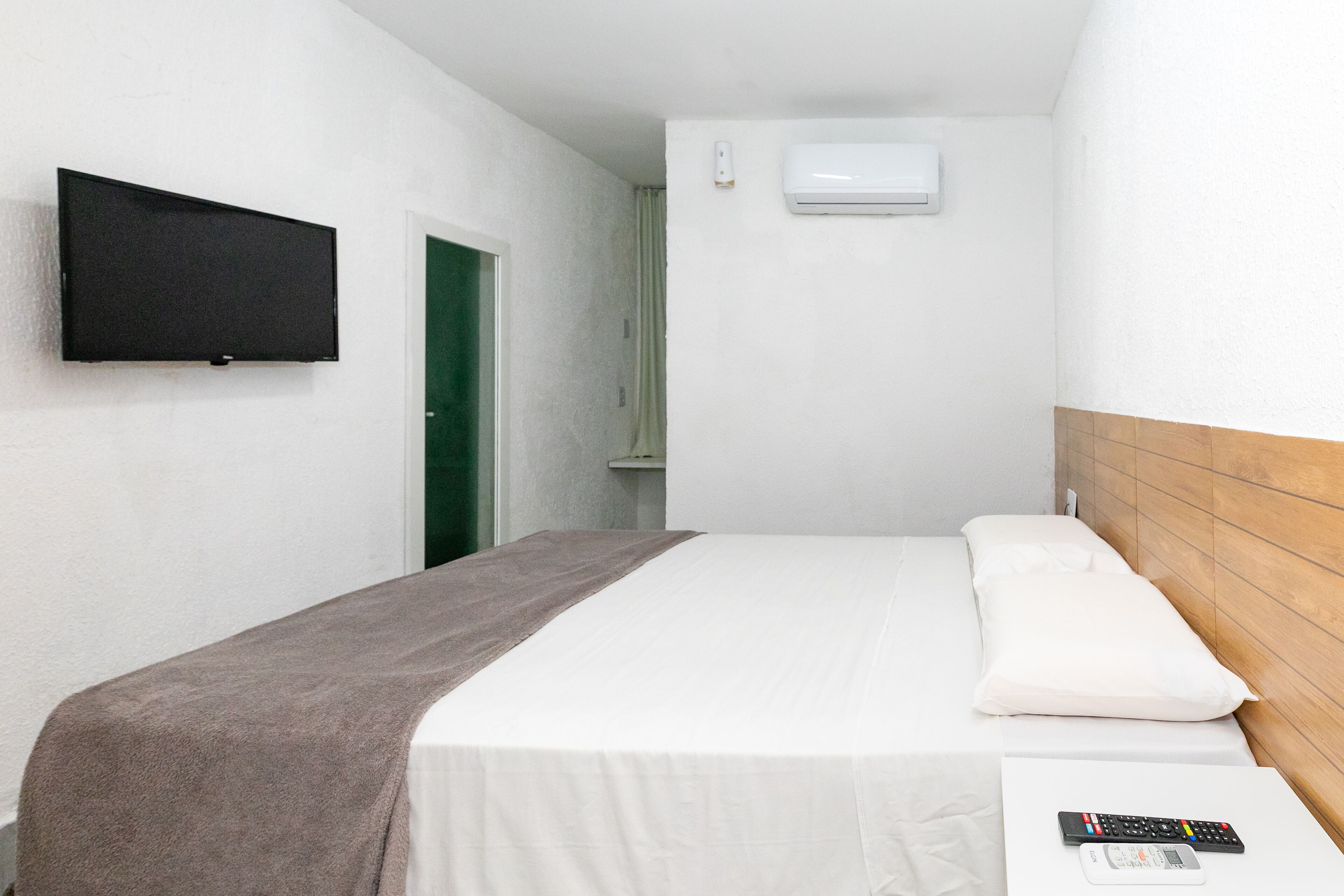 Una camera d'hotel con un letto, una TV a muro, un condizionatore d'aria e una testiera in legno.