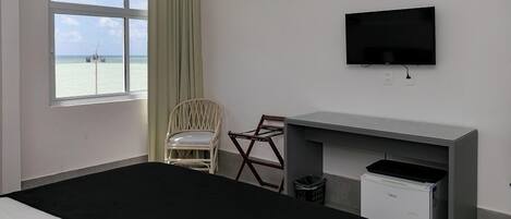 Habitación de hotel con cama, escritorio, silla, televisión y vista al mar.