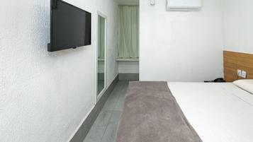 Quarto de hotel com cama, televisão presa na parede, janela com cortina e aparelho de ar condicionado.