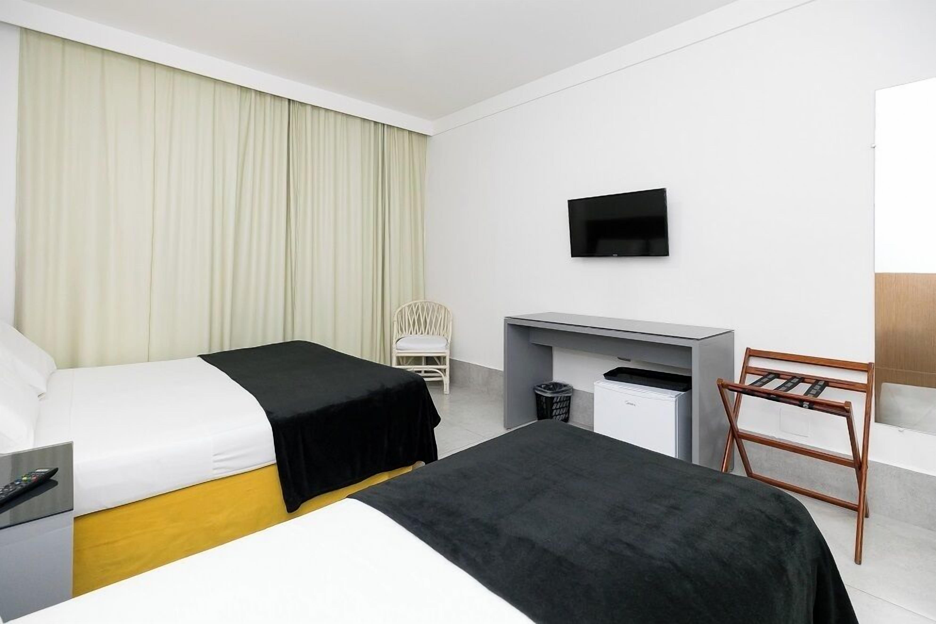 A hotel room with two beds, a desk, a chair, a TV, and a trash bin.