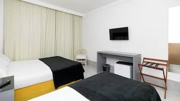A hotel room with two beds, a desk, a chair, a TV, and a trash bin.