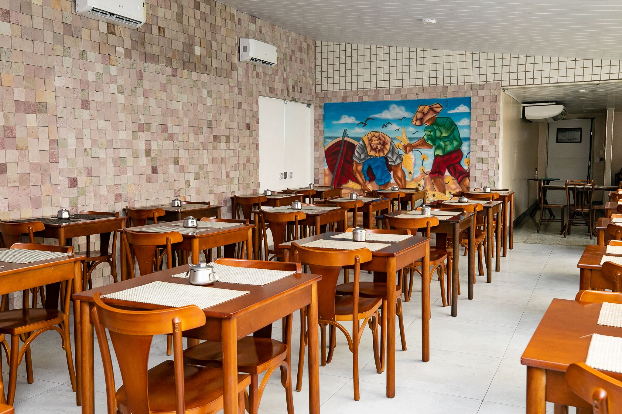 Un comedor con mesas y sillas de madera, un muro de azulejos y un mural en la pared de fondo.