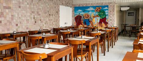 Un comedor con mesas y sillas de madera, un muro de azulejos y un mural en la pared de fondo.