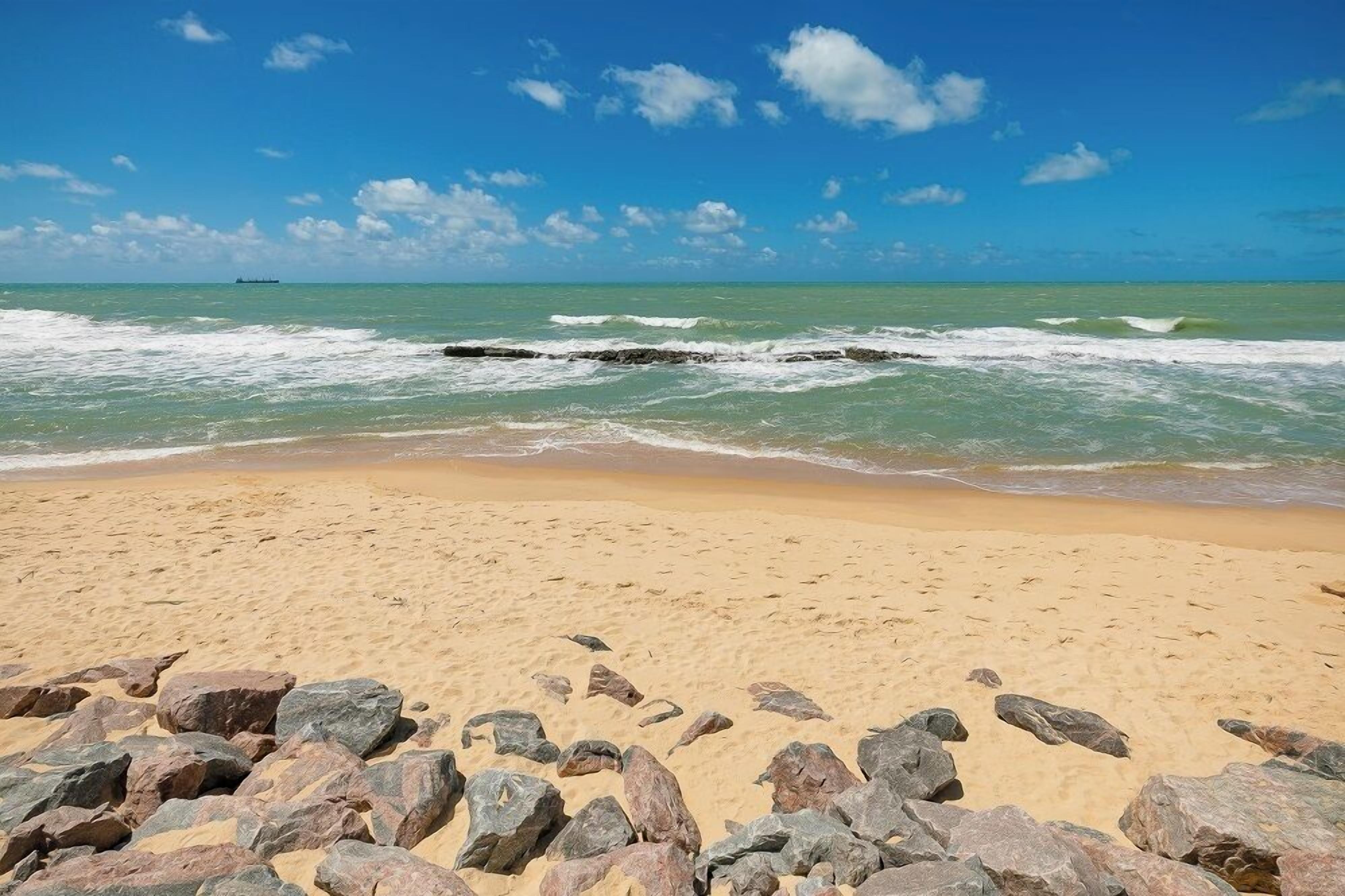A sandy beach with scattered rocks and calm waves.