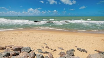 A sandy beach with scattered rocks and calm waves.