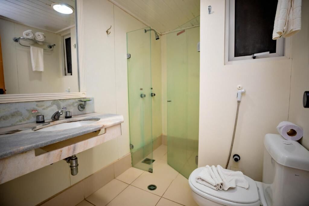A bathroom with a glass-enclosed shower, a sink with a marble countertop, and a toilet with a roll of toilet paper on the wall.