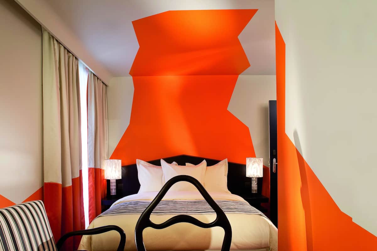 Une chambre d’hôtel avec un lit, des rideaux, une chaise et une table de chevet avec une lampe.