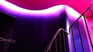 A staircase with a modern design, featuring a metal railing and a curved wall illuminated by purple and pink lighting. - Cristal Champs Elysees (Paris)