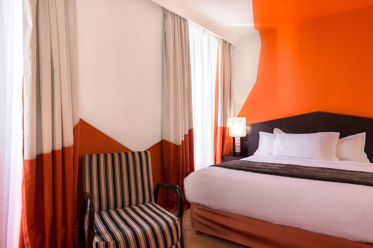 Une chambre d’hôtel avec un lit, un fauteuil à rayures et des rideaux.