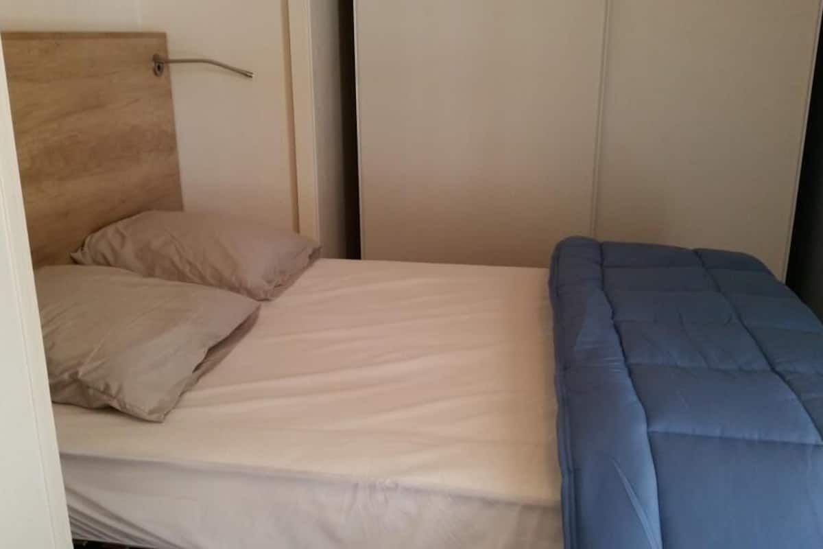 A single bed with a wooden headboard, a beige mattress, and a blue blanket.