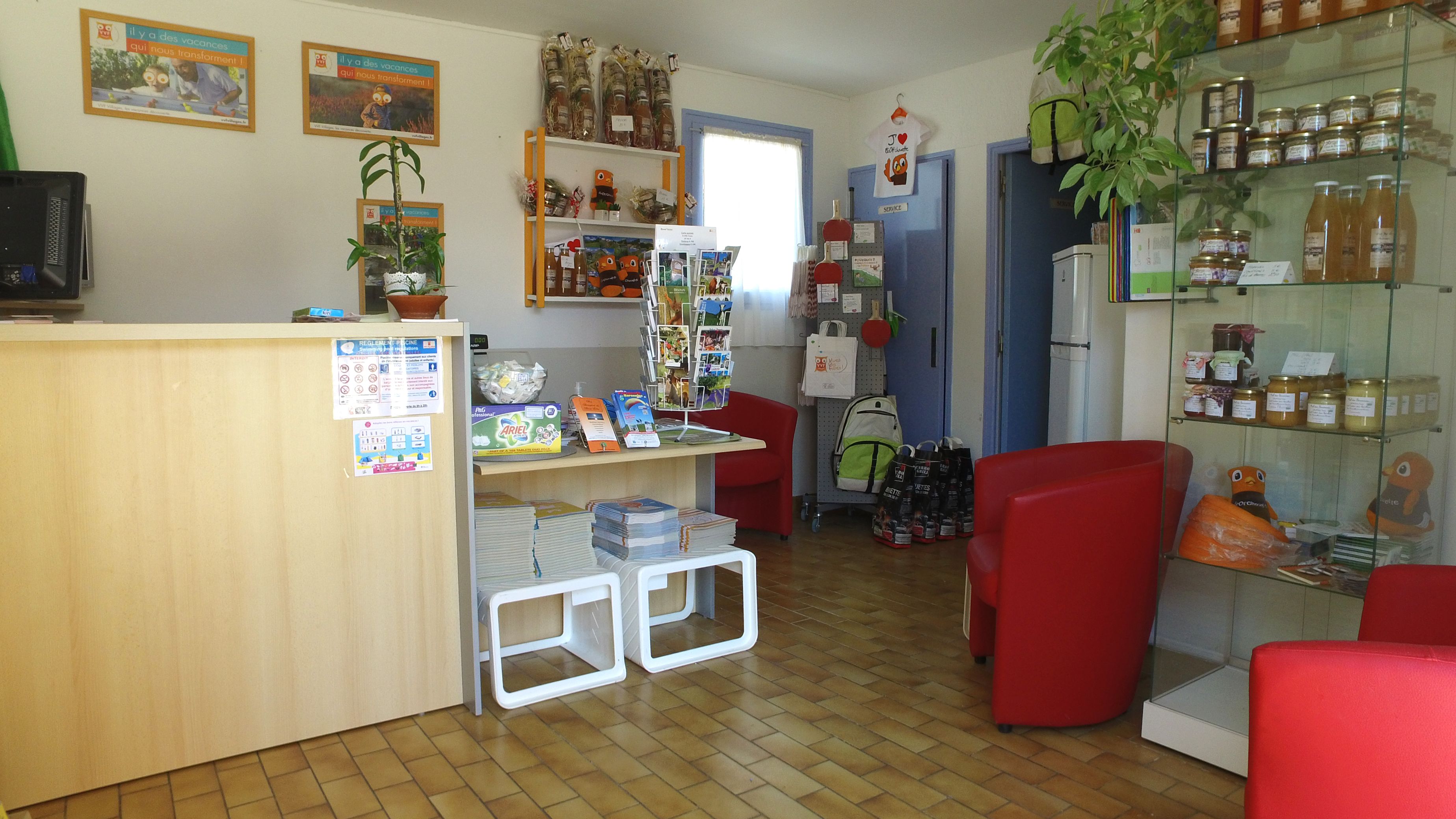 Een receptiegedeelte met een houten balie, rode stoelen, een plant en planken met diverse spullen.